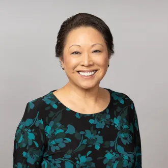 A headshot of Lori Stegmann, smiling and wearing a black and teal floral top.