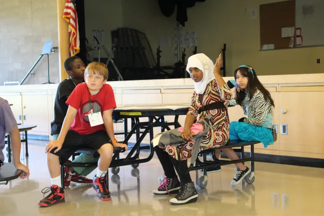 A group of kids participating in the SUN community schools summer camp listen to the list of activities offered for the day: relay races, a cooking class, and piñata-making.