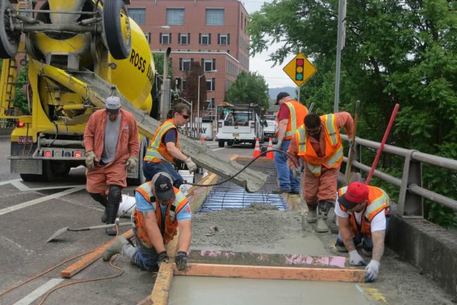 Multnomah County public works employees pour concrete on the sidewalk of the Hawthorne Bridge.