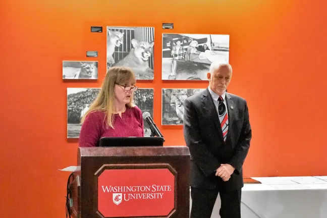 Two people stand at a podium, one is speaking, the other (Mr. Taylor) listens intently.
