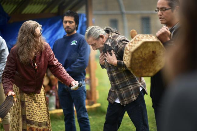 Helper Beth Rakoncay smudges Sundance Chief John Bravehawk with sage and an eagle fan. 