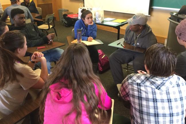 Eight young adults sit in a circle talking.