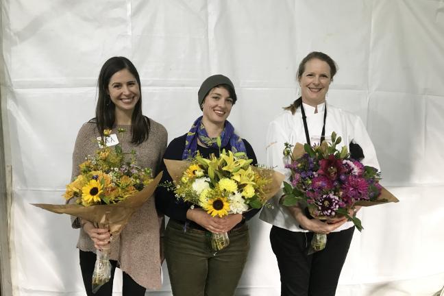 Three women pose with bouquets of fresh flowers