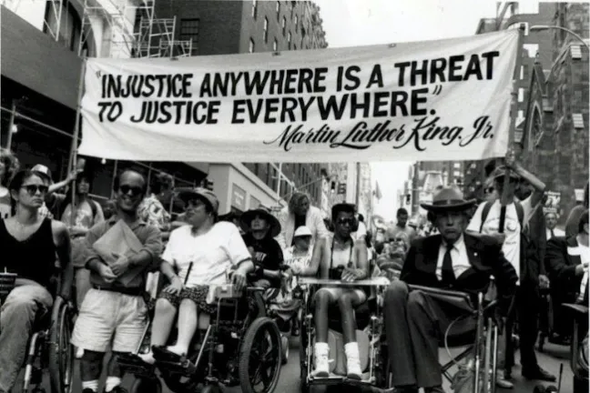 Image of disability rights protesters carrying a banner that says, "Injustice anywhere is a threat to justice everywhere." Dr. Martin Luther King, Jr.