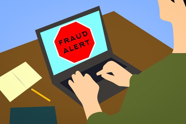 Person at desk with a laptop computer; words on computer screen say, "FRAUD ALERT".