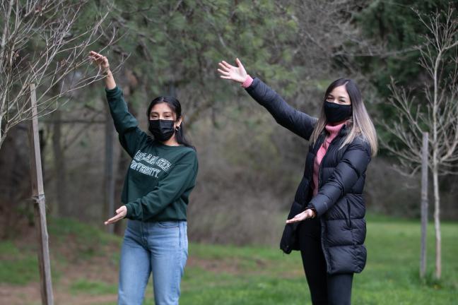 Two people smiling with masks next to a tree