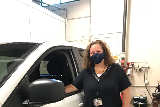 Lee Neils, election worker stands at the door to the white elections van inside the bay area of the building. One of her arms is in the open window. The Multnomah County logo is on the side of the van.