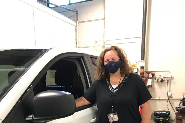 Lee Neils, election worker stands at the door to the white elections van inside the bay area of the building. One of her arms is in the open window. The Multnomah County logo is on the side of the van.  