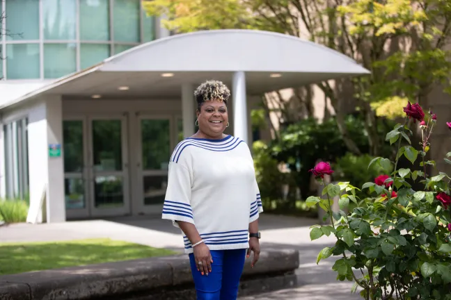 Cynthia Lambert stands in front of a building next to a rose bush