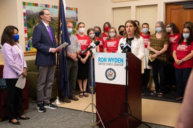 Chair Deborah Kafoury speaking at a podium alongside Commissioner Susheela Jayapal, Oregon Senator Ron Wyden, and members of Moms Demand Action. 