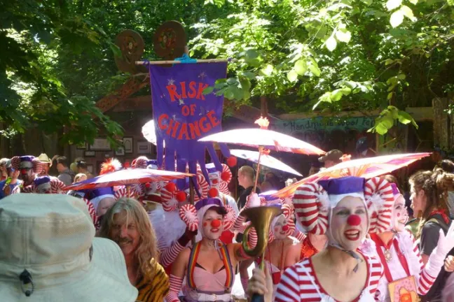 Color photograph of attendees dressed as clowns at the Oregon Country Fair. Someone is holding up a sign that reads "Risk of Change."