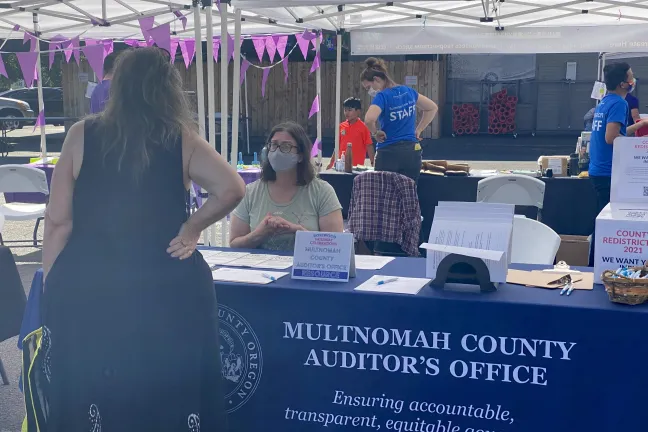 Auditor McGuirk sits at a table at the 9/25/21 Saturday Celebrations event and talks with a community member.