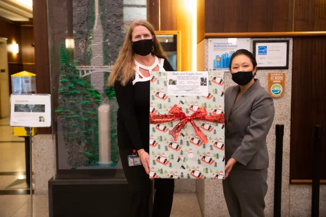 Commissioner Stegmann (right) with staffer hold up a large box covered in holiday wrapping paper
