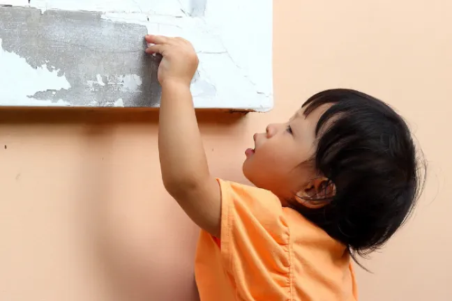 a young child reaches for peeling paint on a window