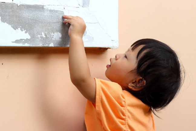 a young child reaches for peeling paint on a window