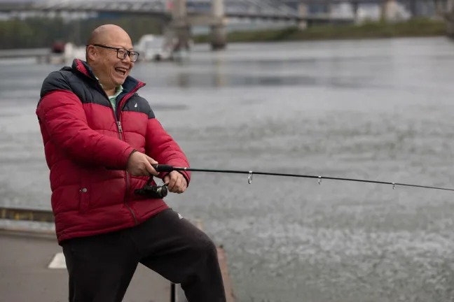 Happy Asian man in a red jacket fishing off a dock in the Willamette River