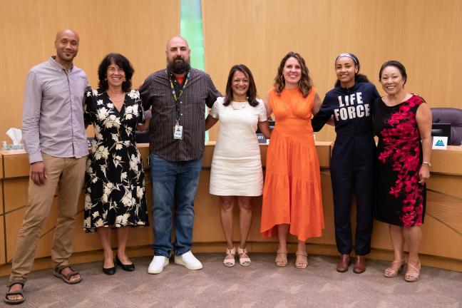 Members of the board, staff from the Multnomah County library and Multnomah Education Service District and Esparanza Spalding pose for a photo in front of the dais in the Multnomah County boardroom.