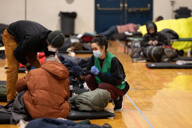 Two shelter workers support someone sleeping in a warming center.