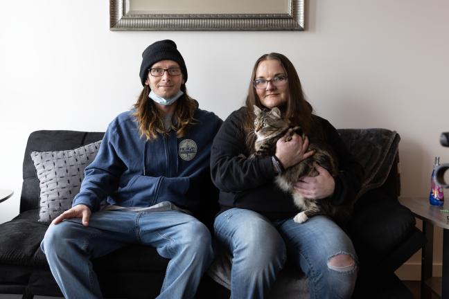 Two people sit on couch with a cat.