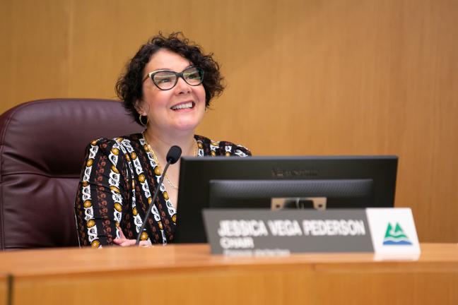 Photo of Jessica Vega Pederson sitting at the dias in the boardroom