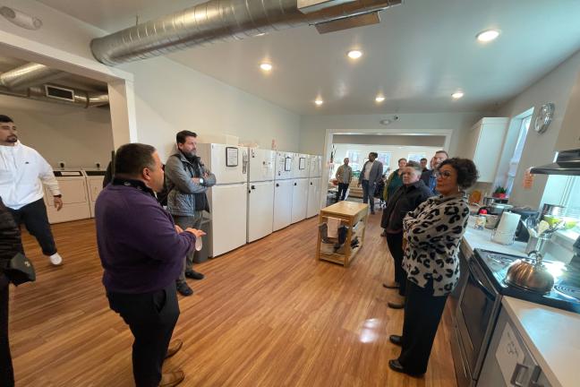 A group of people including Chair Jessica Vega Pederson stands in a kitchen at St. Johns Village.