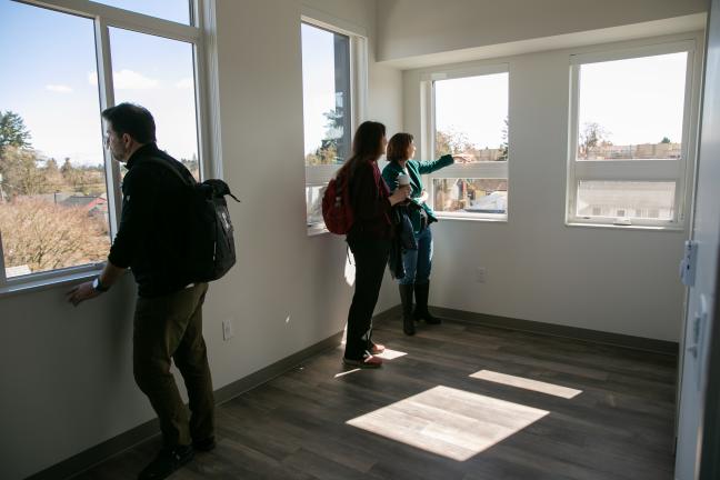 Three people look out windows in an apartment.