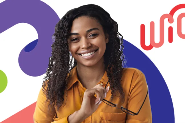 Smiling woman in a brown shirt holding glasses looks welcoming, stands in front of a WIC sign