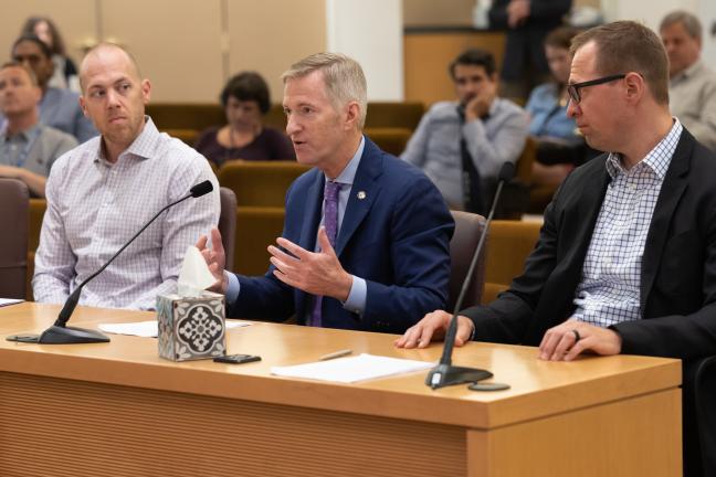 Chris Fick, Mayor Ted Wheeler and Will Glasson sit at a dais in the Multnomah County boardroom.