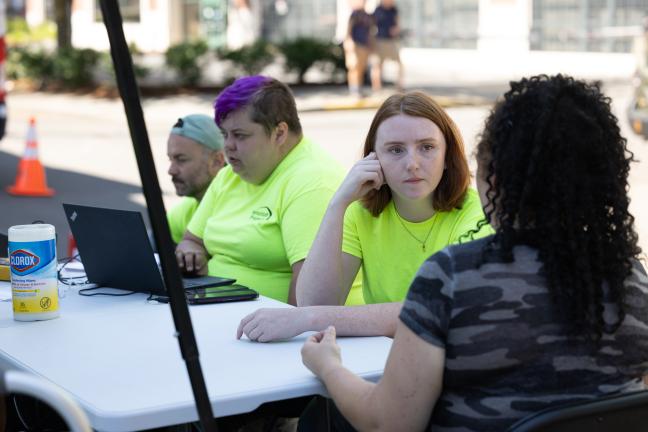 People sitting at a folding table in conversation. Some of them wear yellow Transition Projects shirts.