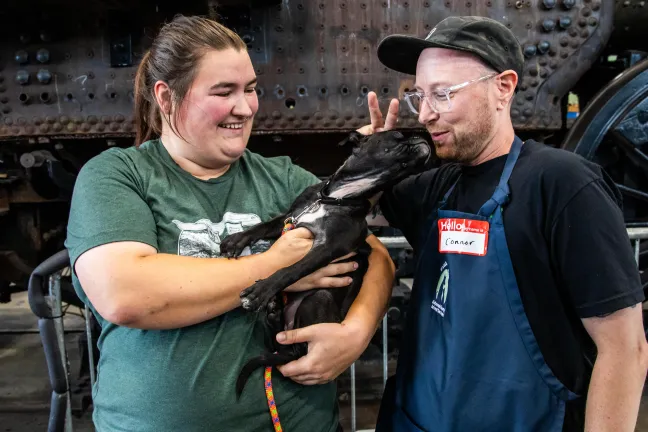 Black puppy, Dahlia, pictured with adopter and foster family.