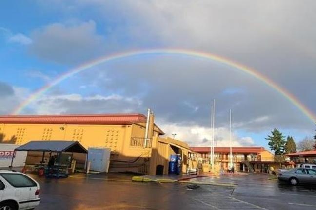 Rainbow over the Rodeway shelter in East Portland - a yellow building with a parking lot in front of it