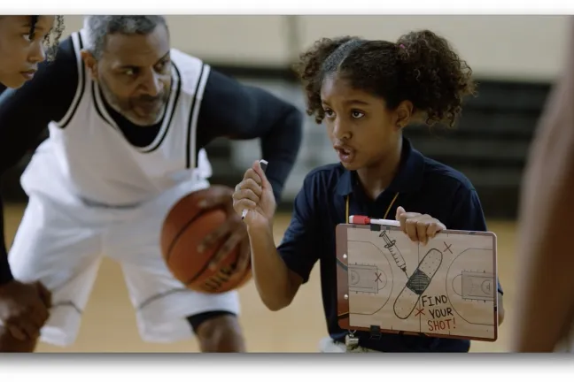 Basketball players huddle around Black girl holding up a tactic board that shows a syringe and bandage, and the message Find Your Shot.