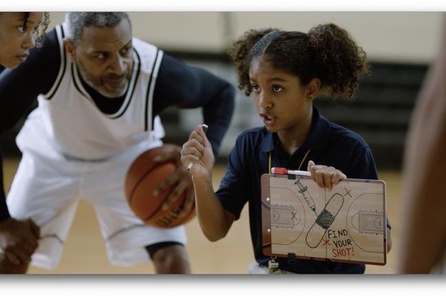 Basketball players huddle around Black girl holding up a tactic board that shows a syringe and bandage, and the message Find Your Shot.