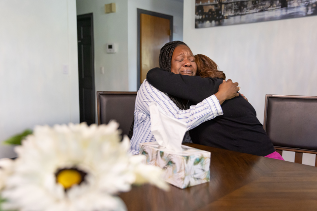 Two women hug at a table.