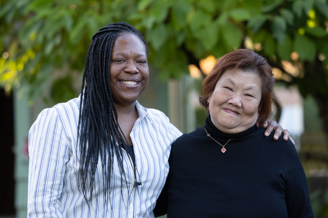 Two women stand next to each other outside.