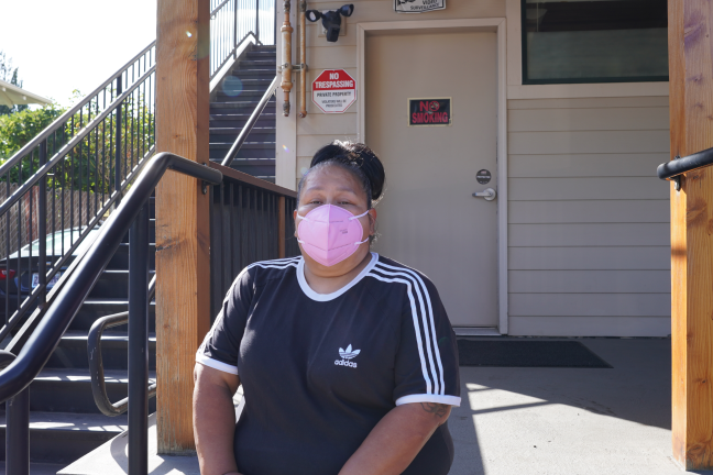 Photo of a woman wearing a pink mask sitting outside a building.