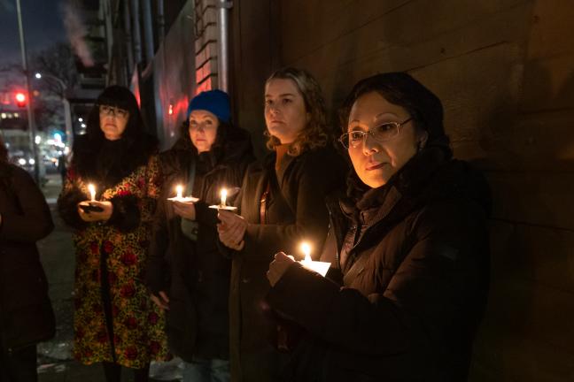 People hold candles while standing outside in the dark.