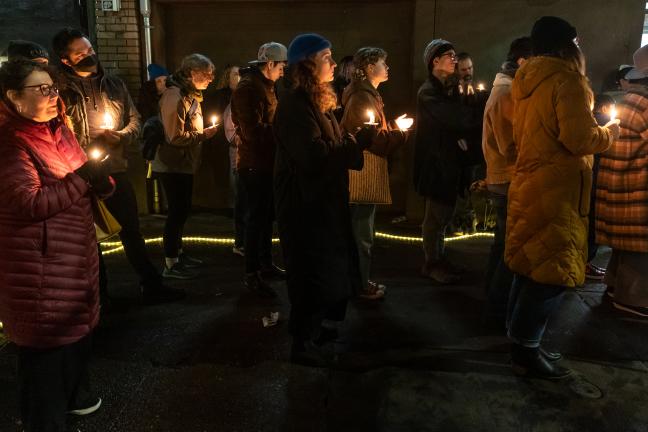 People holding candles stand outside in the dark.