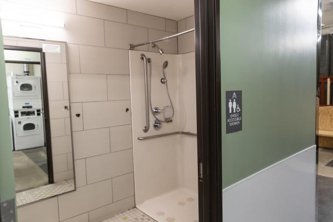 Photo of a shower stall with a laundry room reflected in the mirror.