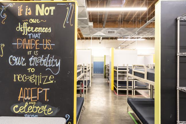 Interior of shelter with beds and a chalkboard wall that says "It is not our differences that divide us, it is our inability to accept and celebrate those"