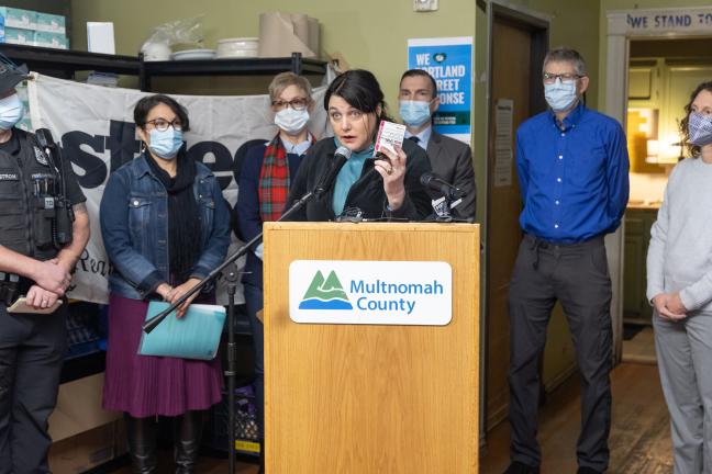 Kaia Sand stands at a dais holding up a box of naloxone.