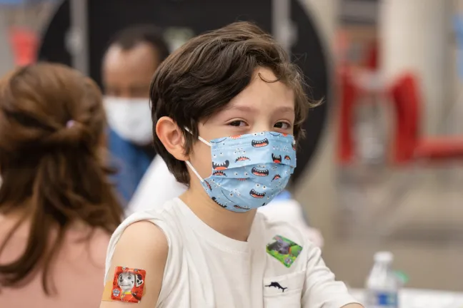 Boy wearing a Paw Patrol sticker over a band aid gives a thumbs up at a catch-up clinic held at McDaniel High School