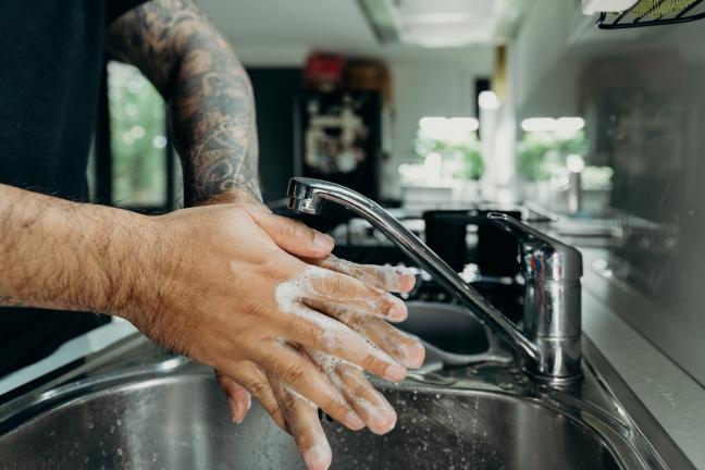 Close up of a man with a tattooed arm washing hands with soap in a sink