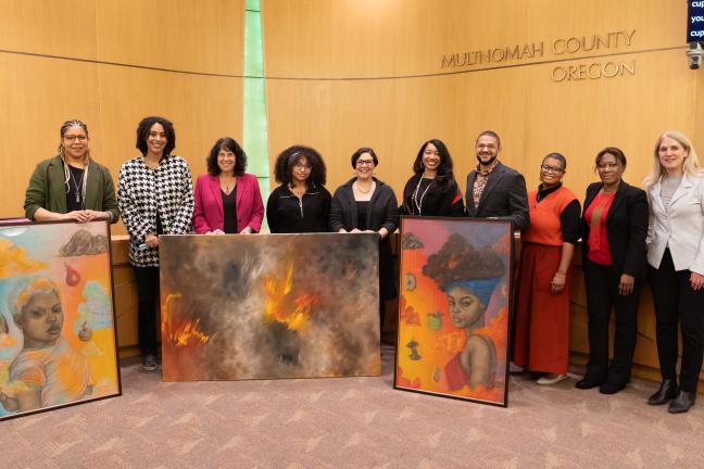 The Board of Commissioners and presenters stand at the dais and hold up three large paintings.