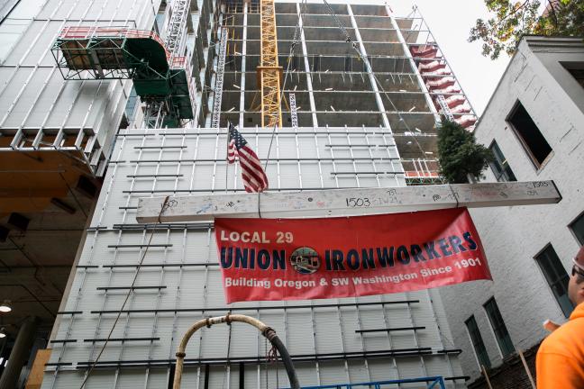Following an ancient tradition started by European builders, a small tree was attached to the beam, to honor the natural resources that contributed to this human-built structure. A U.S. Flag and banner for the local ironworkers union also caught a ride.