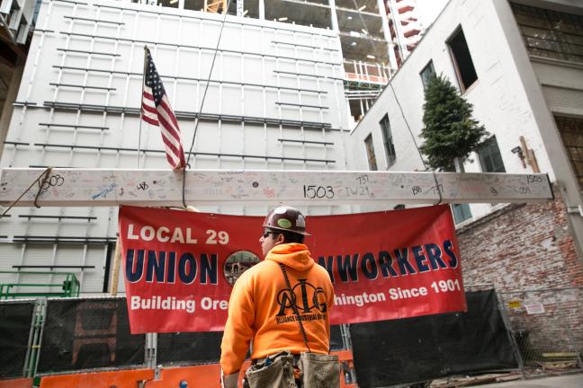 Following an ancient tradition started by European builders, a small tree was attached to the beam, to honor the natural resources that contributed to this human-built structure. A United States flag and a banner for the local ironworkers union