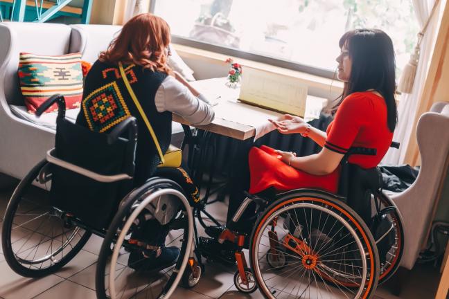 Two people sitting in wheelchairs talking inside a cafe