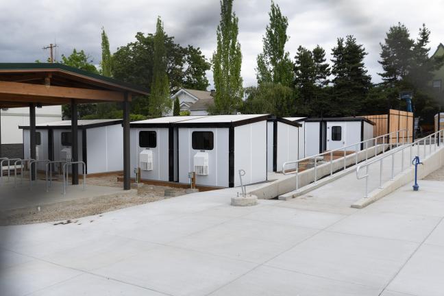 A group of tiny home shelter pods next to an outdoor wheelchair ramp.