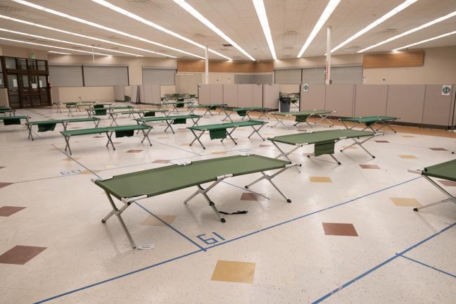 Cots lined up on a tile floor in a large room.