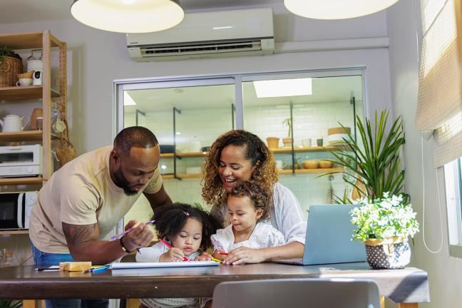 A family enjoys time together at home with a mini split unit behind them on a wall